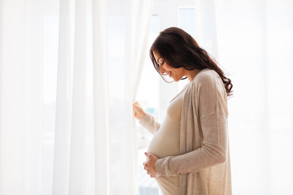 close up of happy pregnant woman with big belly at window