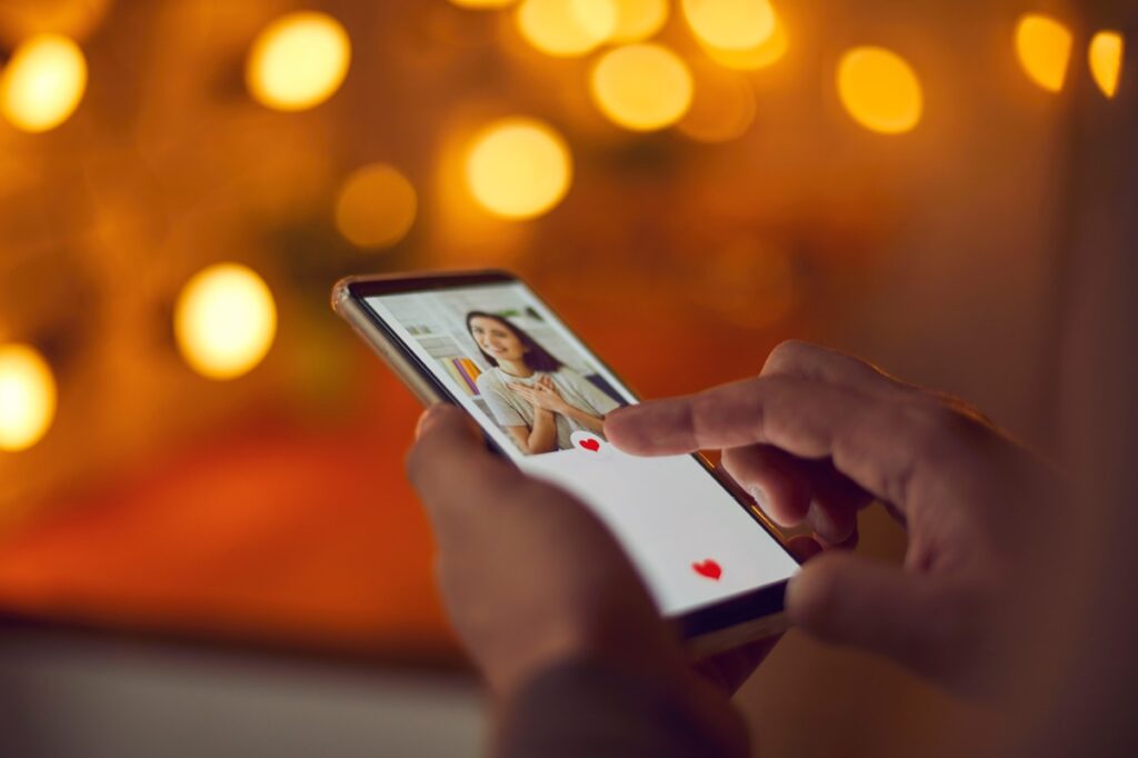 Man holding mobile phone, looking at woman's profile photo on dating app