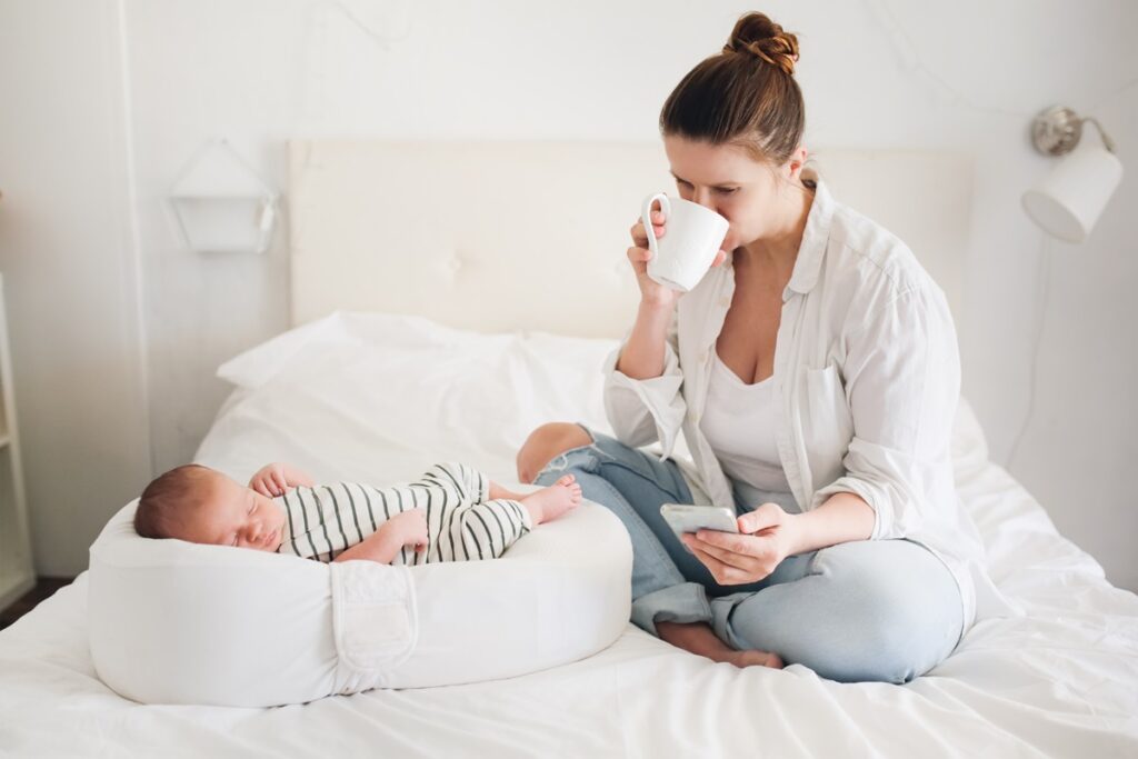 Mother with phone and cup while baby is sleeping