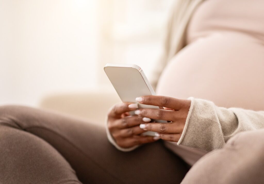 Cropped of pregnant black woman using smartphone while sitting on couch at home.