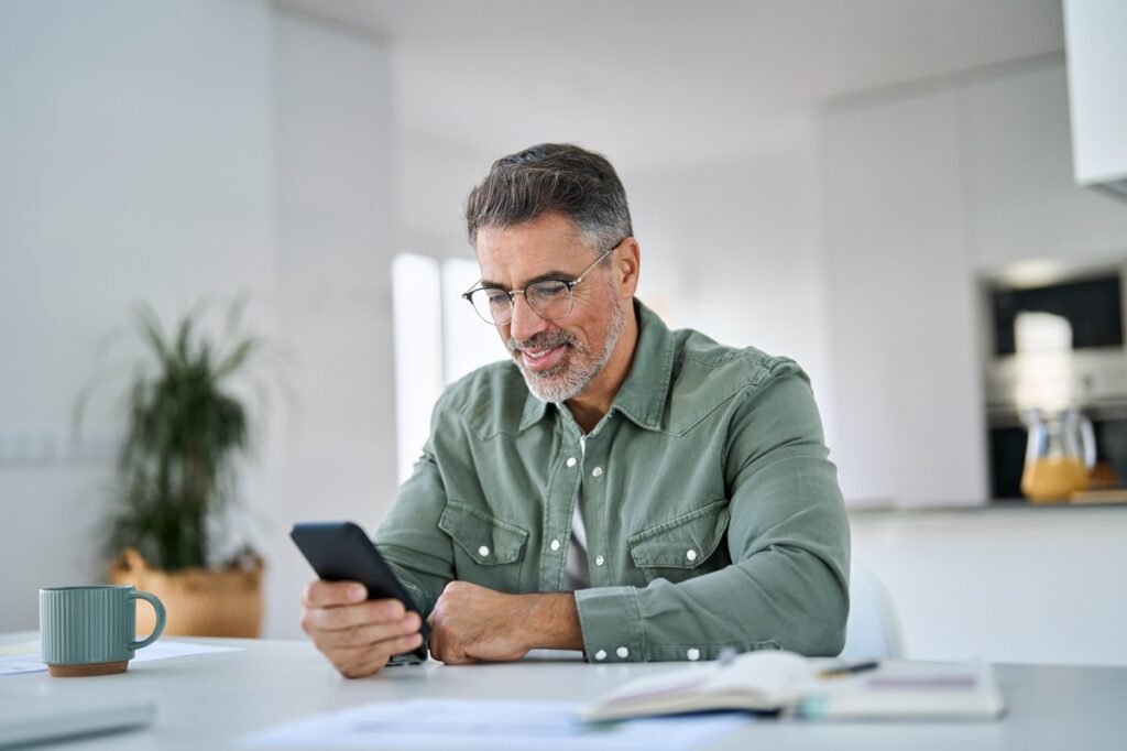 Homem usando celular na cozinha; aplicativos de relacionamento para pessoas mais velhas