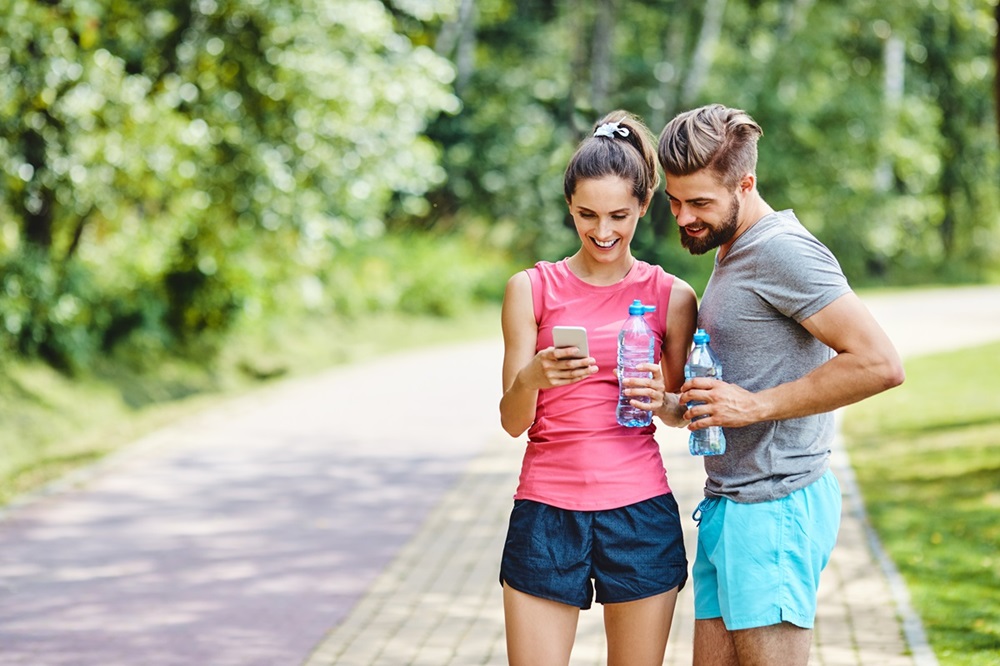 Casal com roupas de ginástica olhando para celular ao ar livre