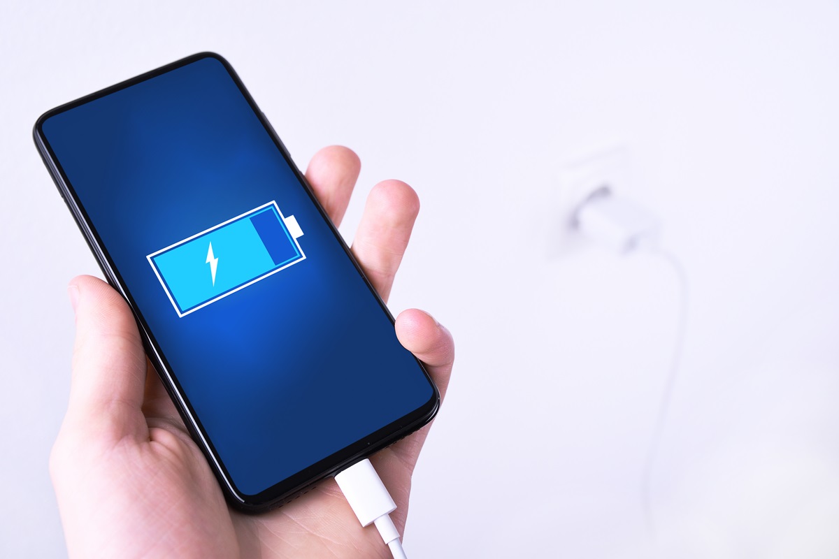 Pessoa segurando celular conectado no carregador; faça a bateria do celular durar mais