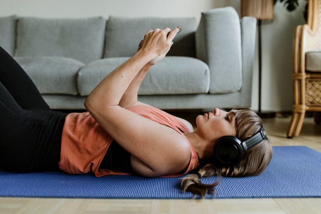 Woman choosing music from her phone while lying on a yoga mat