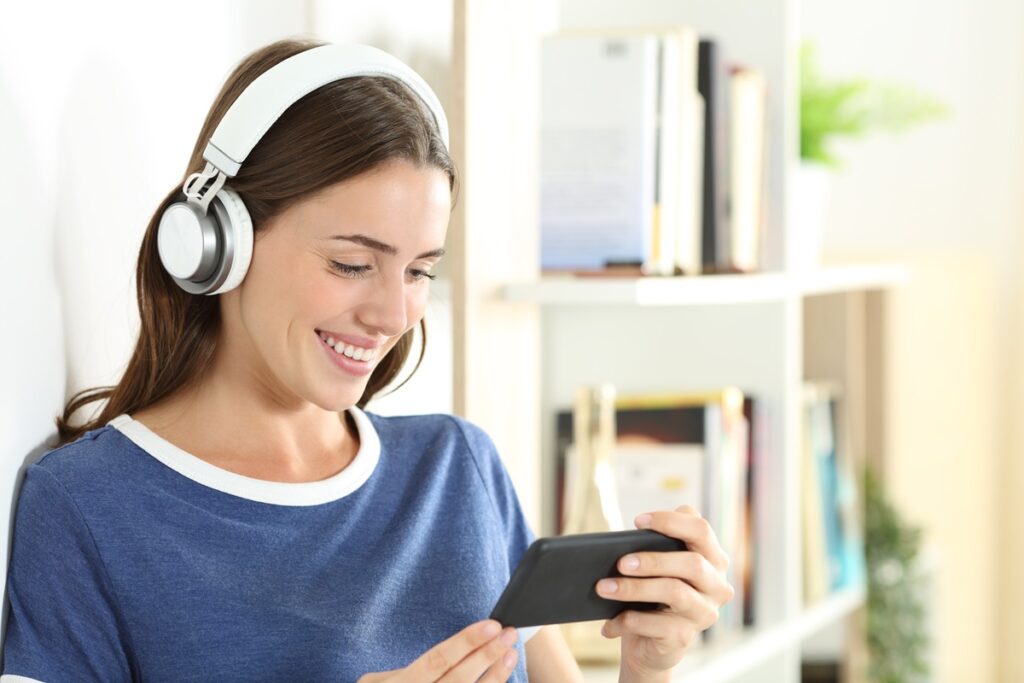 Happy woman watching online videos on smart phone standing at home