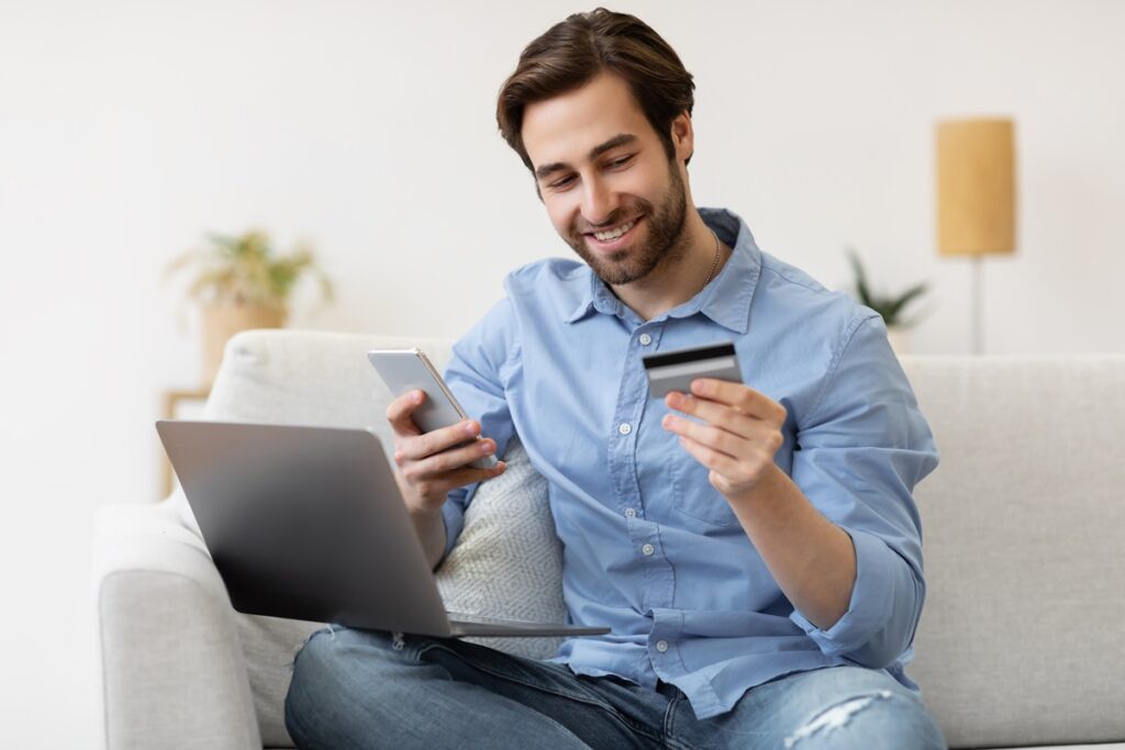 Homem feliz fazendo compras pelo celular e computador com cartão na mão