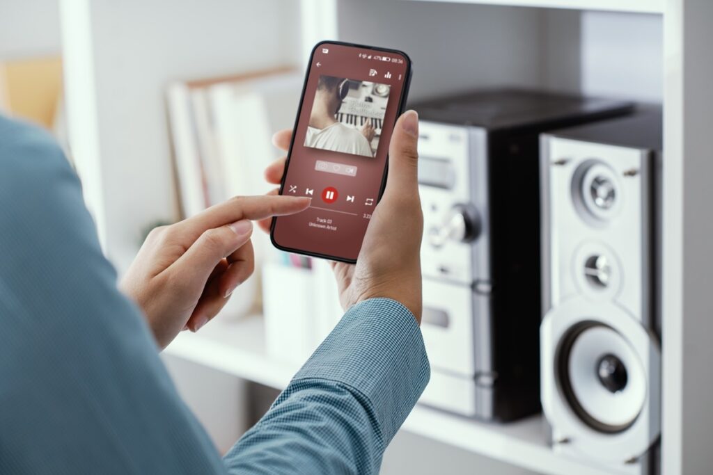 Pessoa segurando celular com app de música, com rádio de fundo