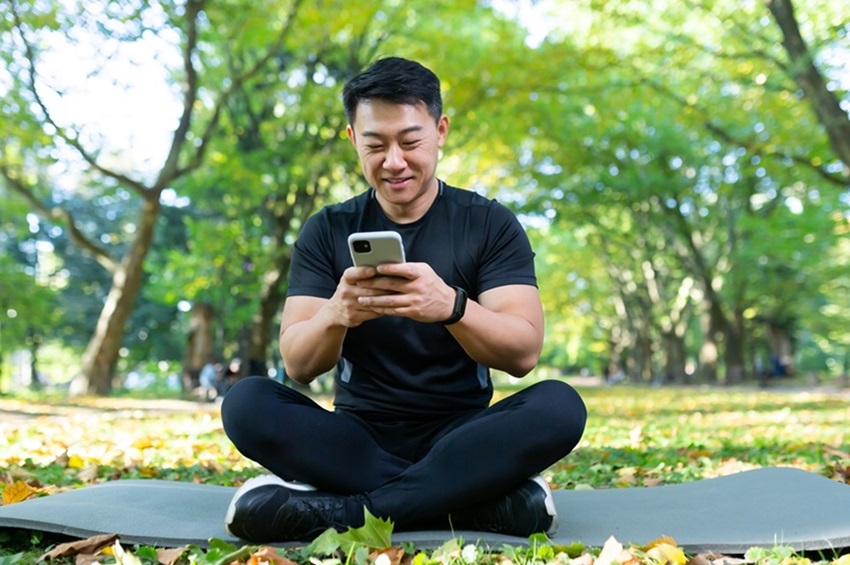 Homem usando celular com app para fazer yoga no parqu