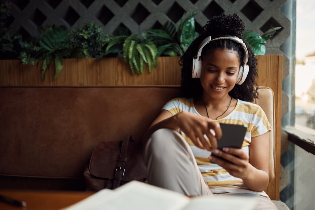 Mulher escutando música com headphone em café, segurando celular